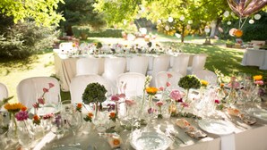 Une longue table de banquet installée à l’extérieur, agrémentée de chaises blanches, de verres et de compositions florales.