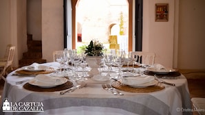 Une table à manger dressée pour un repas, avec une nappe blanche, des assiettes, des couverts et des verres.