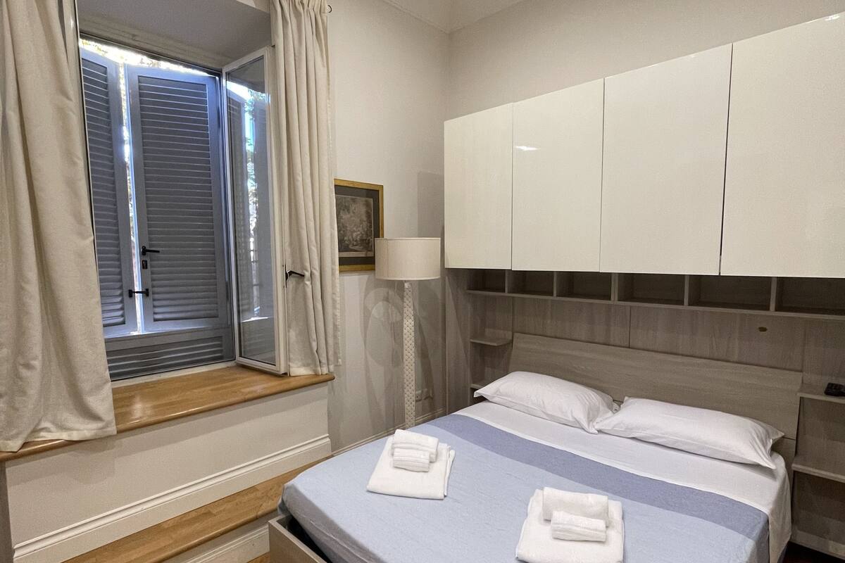 Une chambre à coucher avec un lit, une fenêtre avec des rideaux, une lampe de chevet et une armoire.