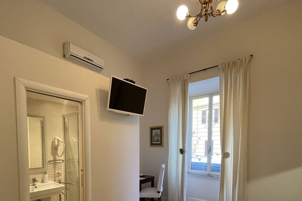 Une chambre d’hôtel équipée d’un lit, d’un bureau, d’une chaise, d’un téléviseur fixé au mur et d’une fenêtre avec des rideaux.