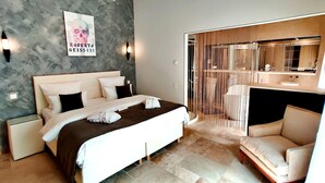 Une chambre d’hôtel moderne avec un grand lit, une table de chevet, une chaise, une salle de bain avec un miroir et un espace douche.