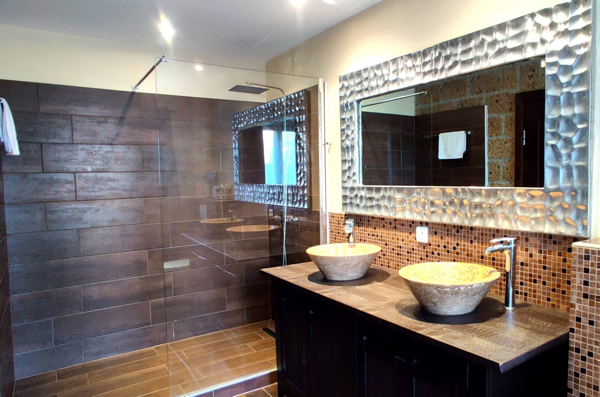 A modern bathroom with a large mirror, two sinks, and a shower area.