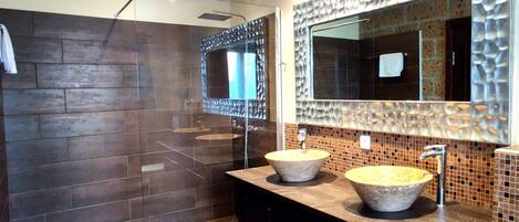 A modern bathroom with a large mirror, two sinks, and a shower area.