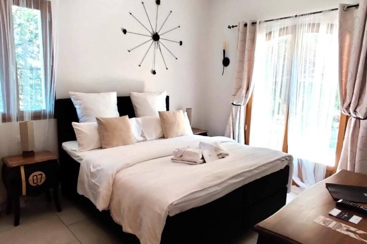 A neatly made bed with white bedding and a black headboard, a bedside table with a number, and a wall clock.