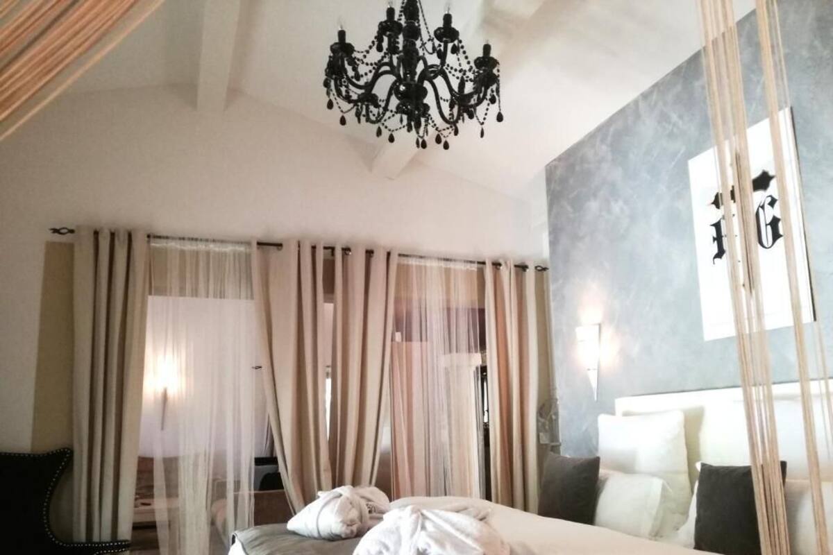 A hotel room with a bed, a chandelier, sheer curtains, and a large mirror.