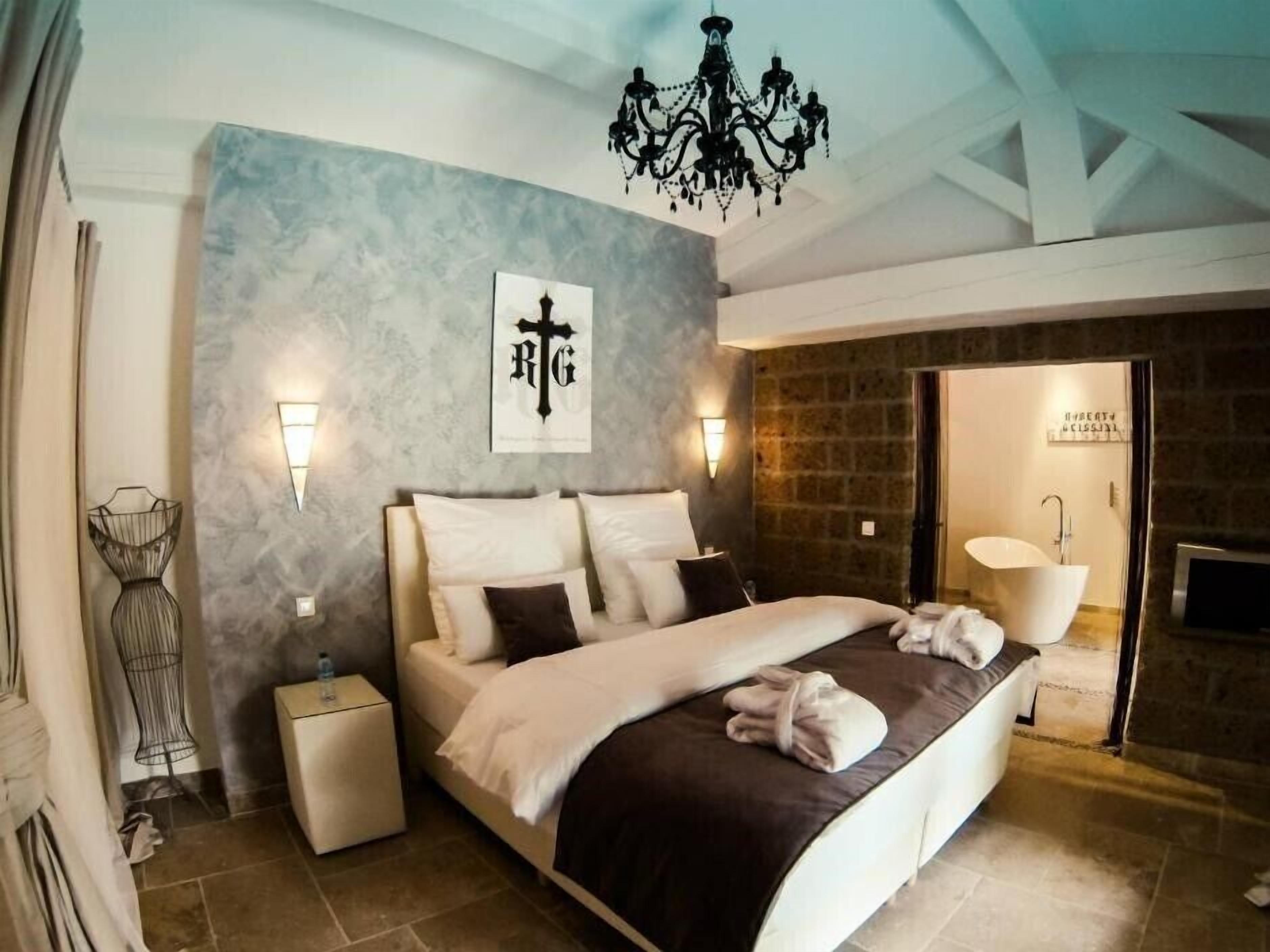 A modern bedroom with a large bed, a chandelier, a stone wall, and a sign indicating a spa area.