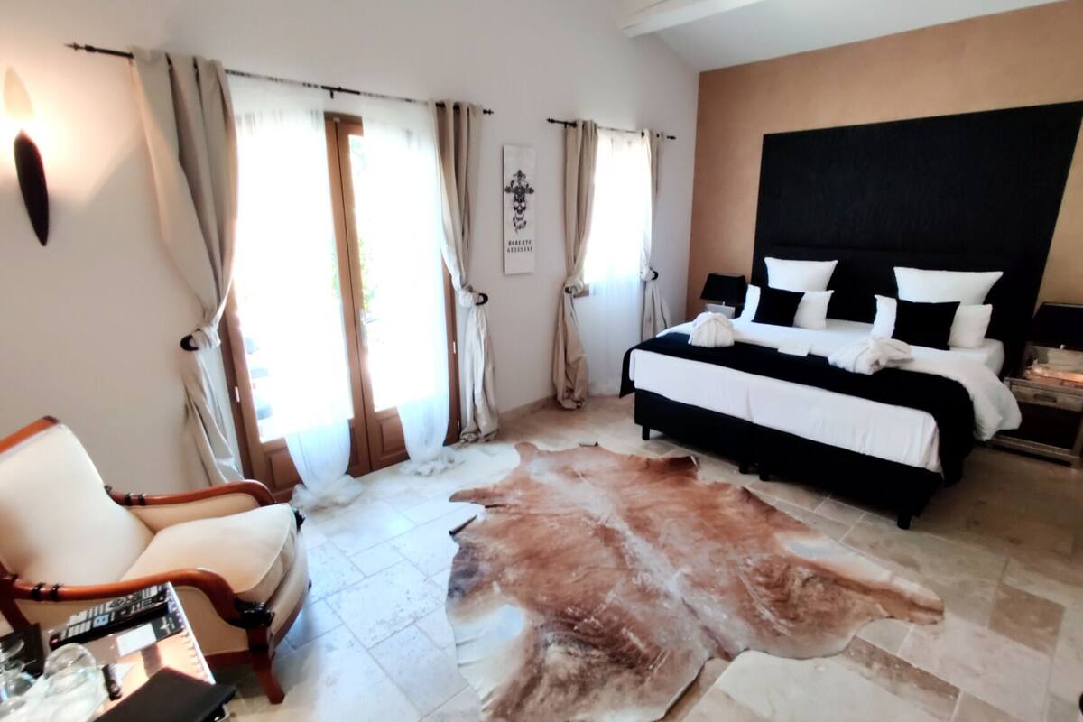A bedroom with a large bed, a chair, a cowhide rug, and curtains.