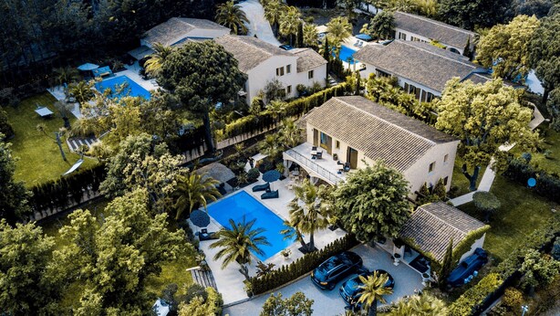 Vue aérienne d’une propriété résidentielle comprenant plusieurs bâtiments, une piscine et une végétation luxuriante.