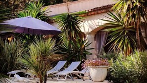 Un espace piscine équipé de chaises longues, d’un grand parasol et d’un escalier menant à un bâtiment dont le toit est recouvert de tuiles.