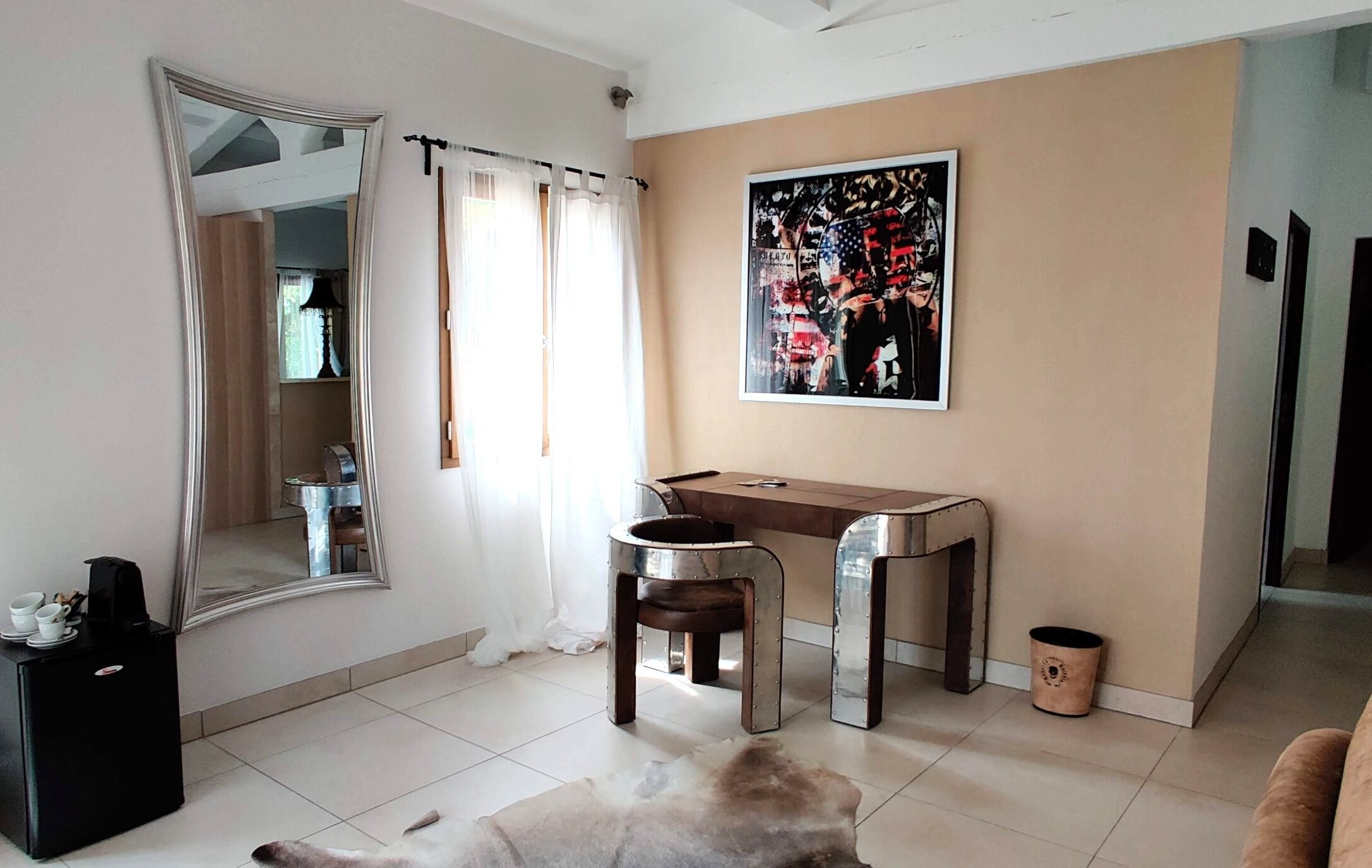 Una habitació amb un mirall gran, un escriptori amb dues cadires, un quadre a la paret i una catifa petita al terra.
