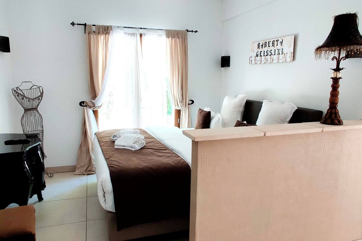 A hotel room with a bed, a desk, a chair, a lamp, and a wall-mounted TV.