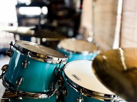 Primer plano de tambores turquesa con herrajes cromados, probablemente en un estudio de música o sala de ensayo.