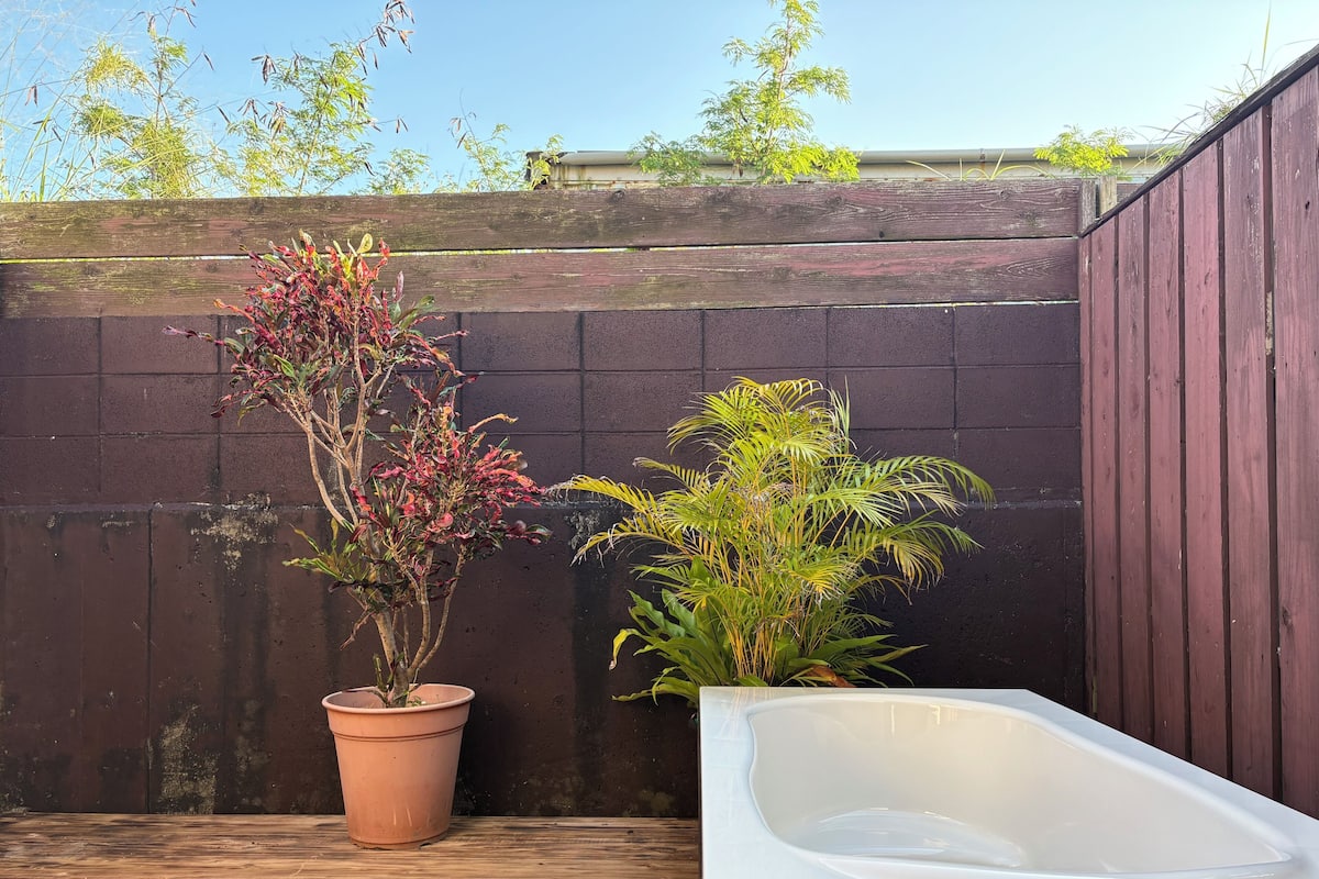 A wooden deck with a white bathtub and two potted plants.