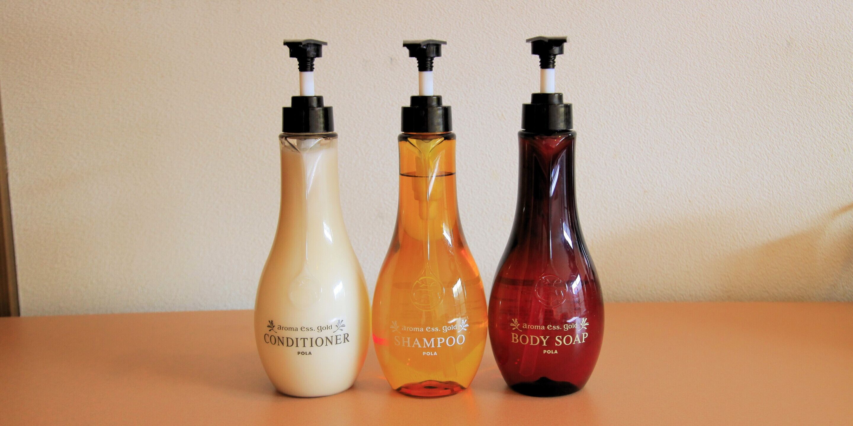 Three bottles of conditioner, shampoo, and body soap on a table.