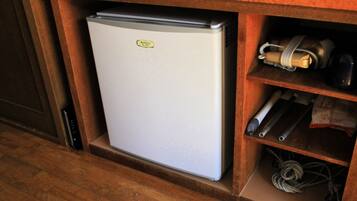A compact refrigerator in a wooden cabinet with a small shelf containing a bag of snacks and a coiled cable.