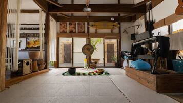 A spacious room with a high ceiling, wooden beams, a large window, and a variety of items including a blue plush toy, a drum, and a guitar.