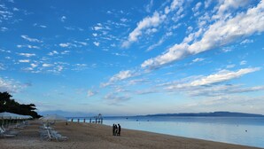 Una playa con filas de tumbonas y sombrillas, un mar tranquilo y un cielo despejado con algunas nubes.