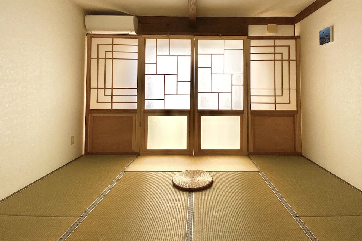 A traditional Japanese room with tatami flooring, sliding doors, and a tatami mat in the center.