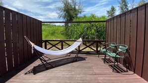 Una terraza de madera con una hamaca y dos sillas, rodeada por una cerca de madera y follaje.