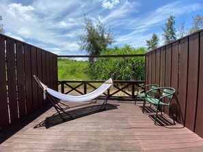 Una terraza de madera con una hamaca y dos sillas, rodeada por una cerca de madera y follaje.