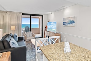 A modern living room with a view of the ocean, a dining area, and a painting on the wall.