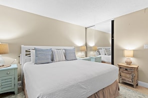 A bedroom with a large bed, bedside tables, a mirror, and a dresser.