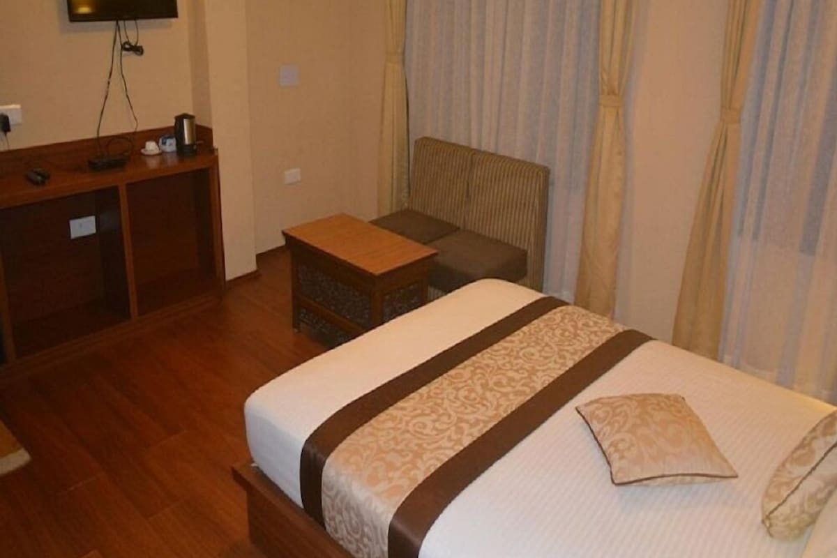 A hotel room with a bed, a desk, a chair, and a television mounted on the wall.