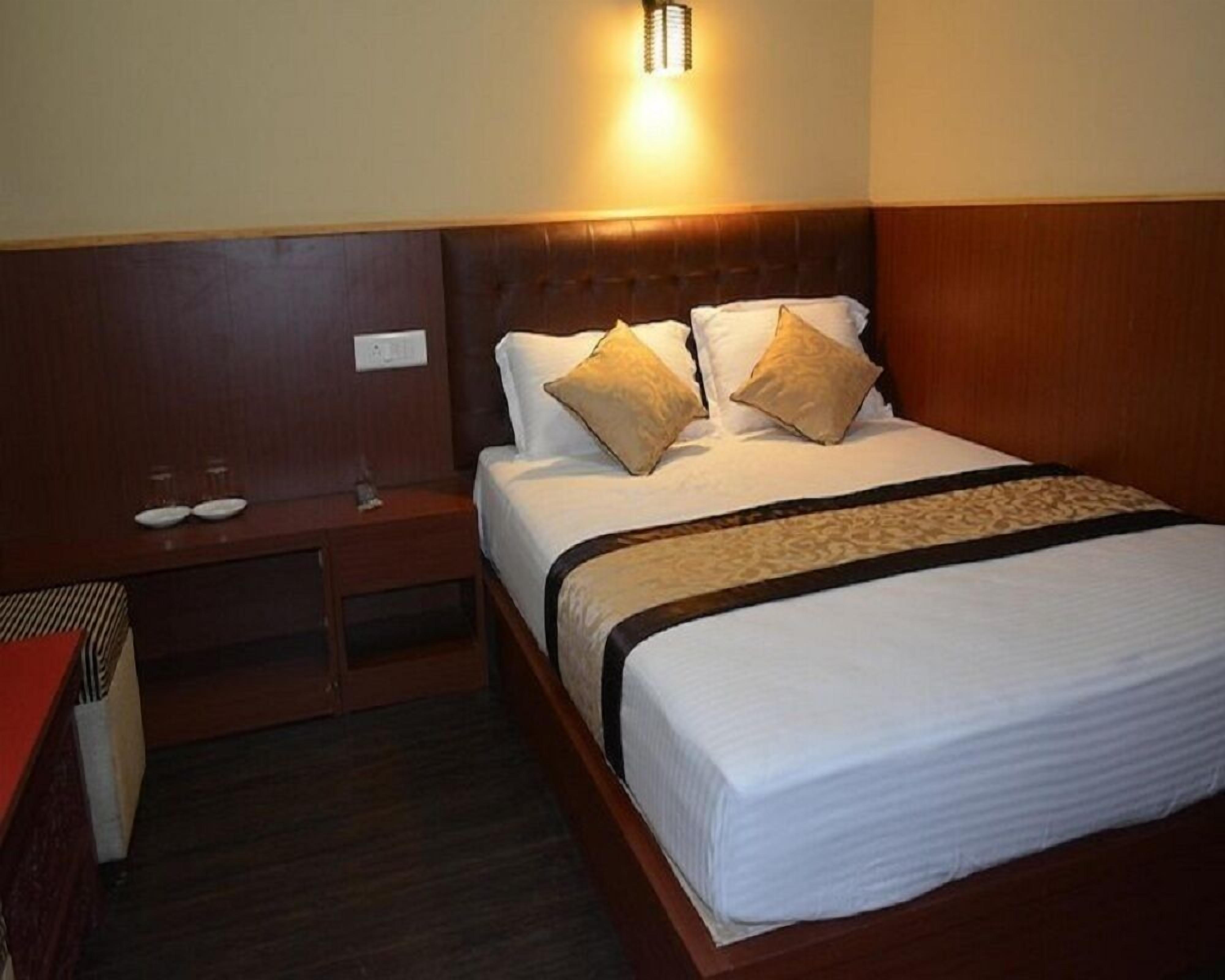 A hotel room with a large bed, a nightstand with a lamp, and a wall-mounted light.