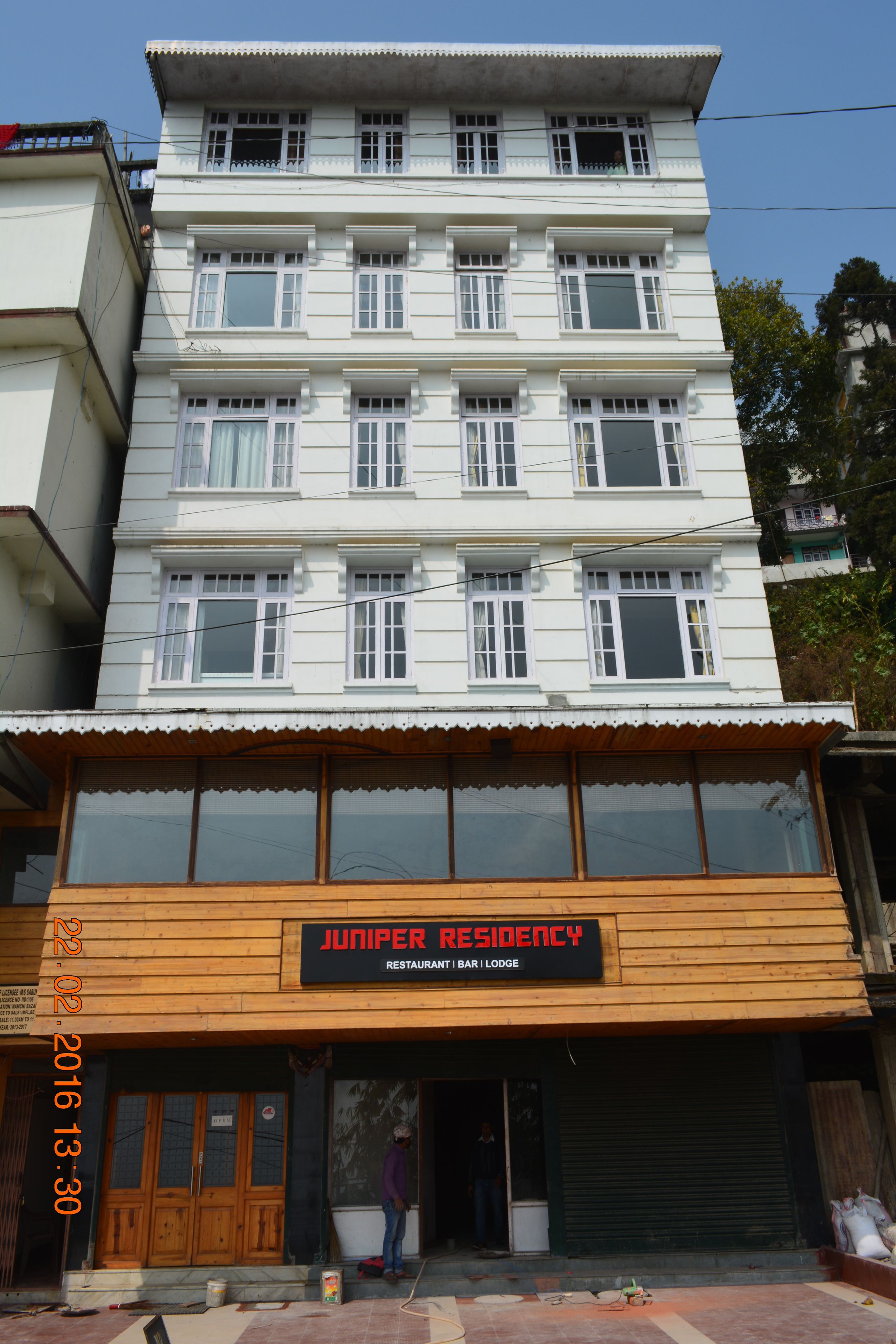 Un edificio de varios pisos con un letrero que indica 'Juniper Residency', donde se encuentra un restaurante, bar y hospedaje.
