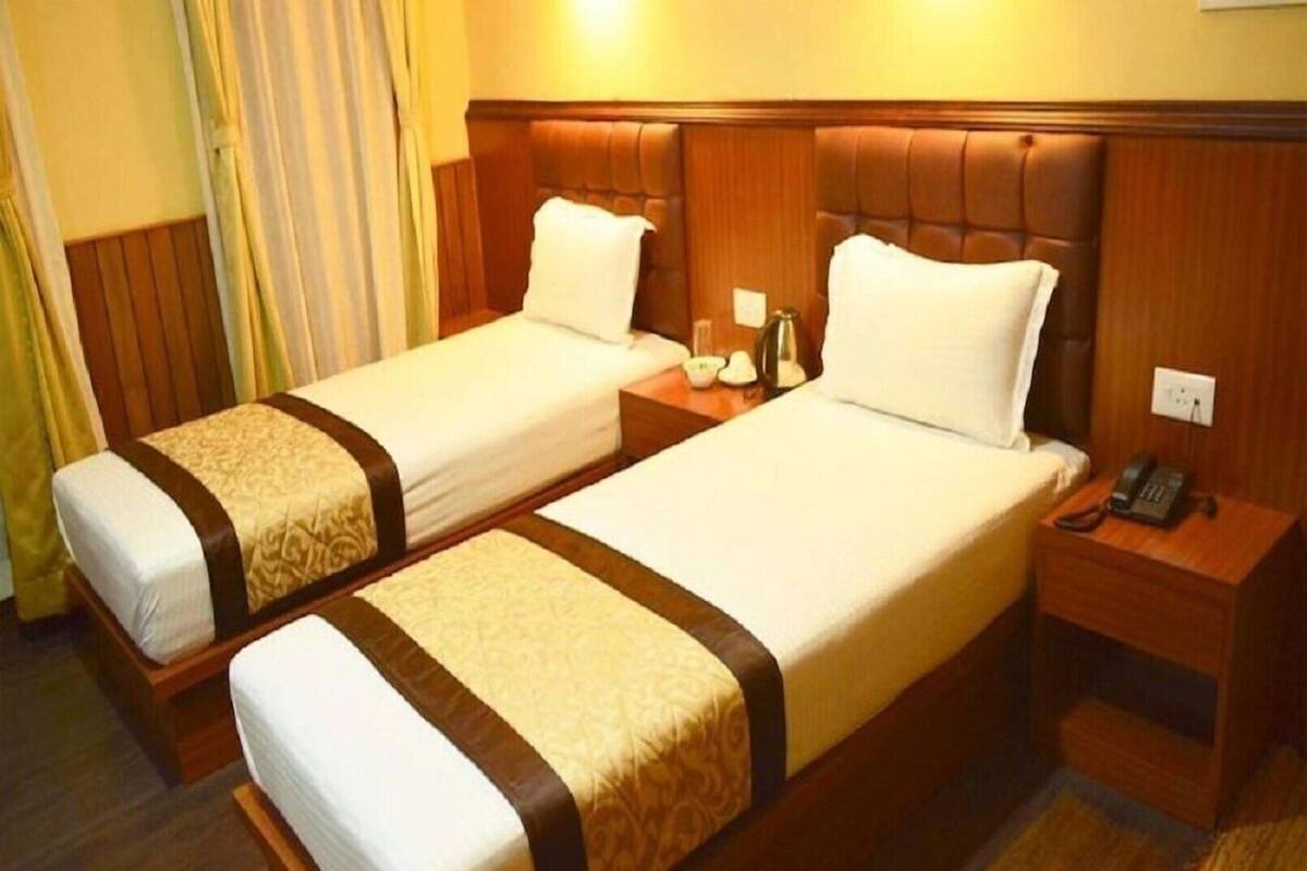 A hotel room with two single beds, wooden headboards, bedside tables with lamps, and a telephone.