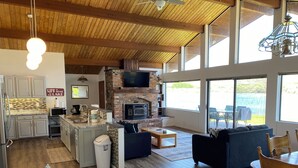 A spacious living area with a kitchen, a fireplace, and large windows offering views of the outdoors.