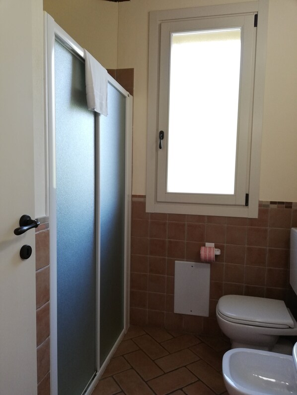 A bathroom with a shower, toilet, and a window.