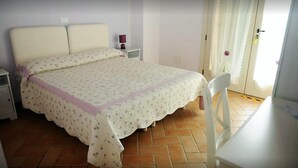 Un dormitorio con cama, mesitas de noche, una silla y una puerta con cortinas.
