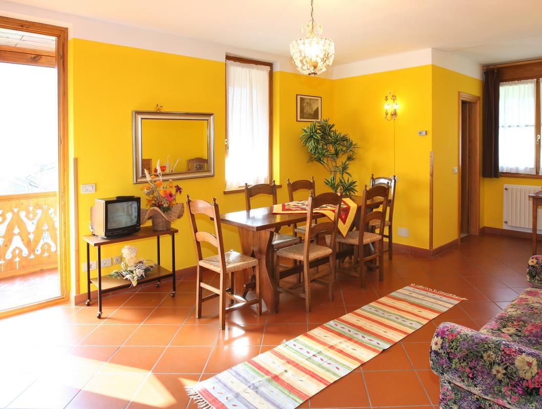 A dining area with a table and chairs, a television on a stand, and a plant.