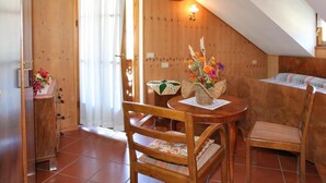 A cozy room with wooden walls, a dining table with chairs, a bed with a colorful blanket, and a window with curtains. - Casa Gilda (Falcade)
