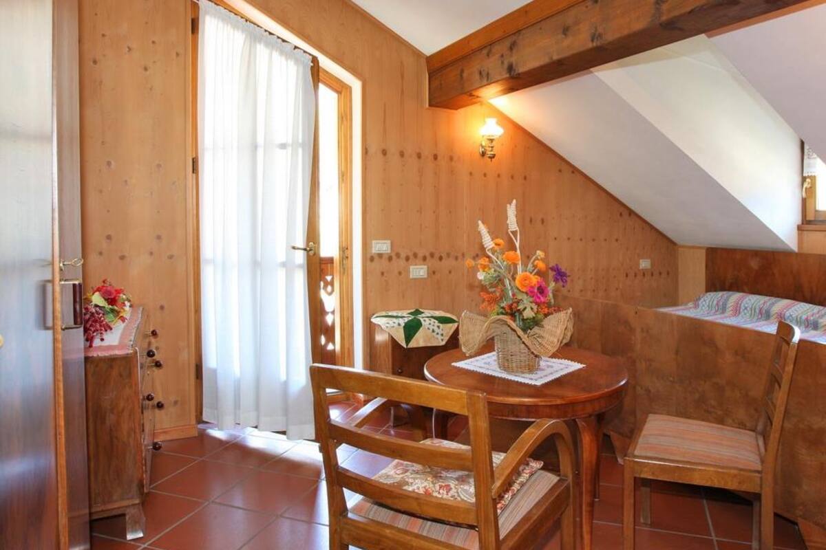 A cozy room with wooden walls, a dining table with chairs, a bed with a colorful blanket, and a window with curtains.