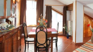 A dining area with a wooden table, chairs, and a vase of flowers. - Casa Gilda (Falcade)