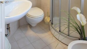 A modern bathroom with a white sink, toilet, and glass shower enclosure. - Casa Gilda (Falcade)