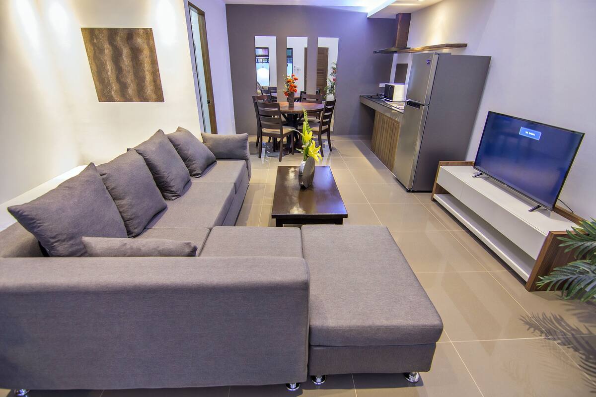 A modern living room with a sectional sofa, a flat-screen TV, and a dining area with chairs and a table.