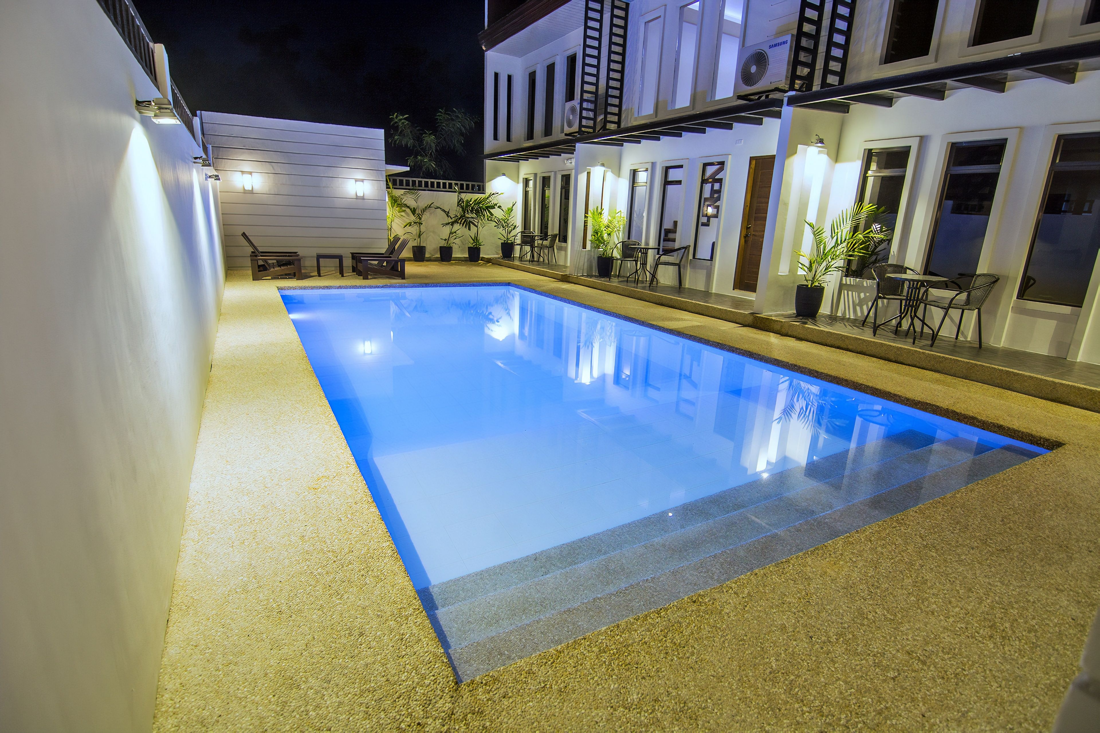 A rectangular swimming pool with a clear blue water surface, surrounded by a sandy area.