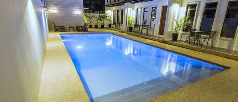 A rectangular swimming pool with a clear blue water surface, surrounded by a sandy area.
