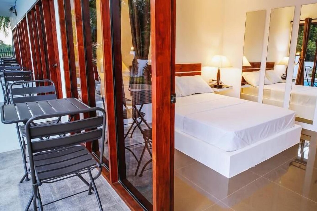 A hotel room with a bed, two bedside tables, a mirror, and a seating area with tables and chairs.