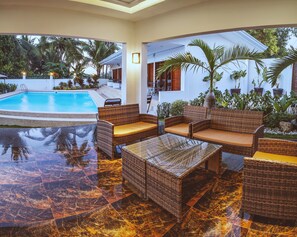 Un espace aménagé au bord de la piscine, avec des meubles en osier et un sol en marbre.