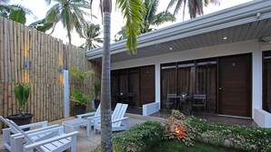 A modern outdoor patio with white lounge chairs, a bamboo fence, and a small garden area with plants and a decorative light. - Quest Villa (Panglao)