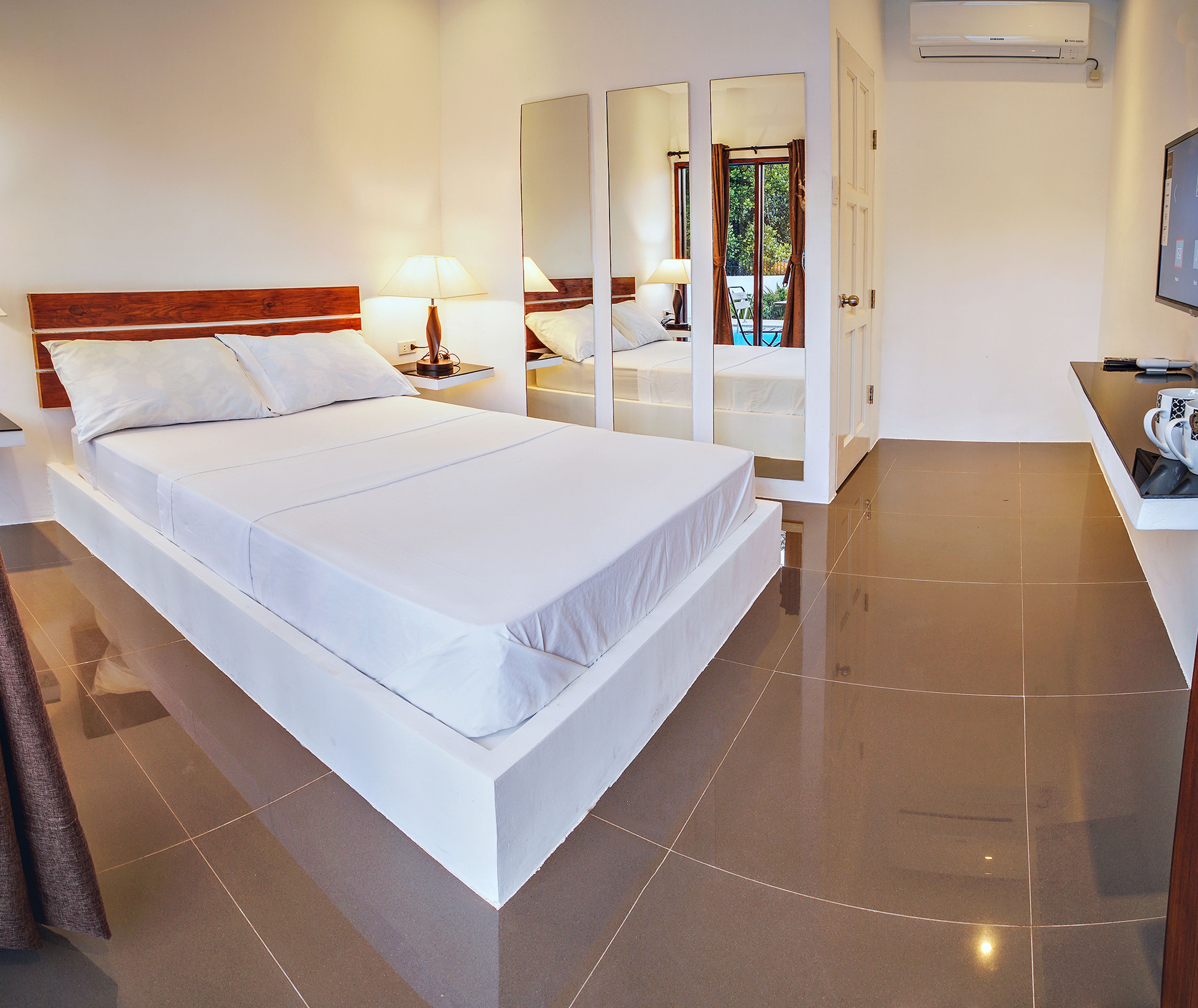 A modern hotel room with a large bed, a bedside table with a lamp, a wardrobe, and a TV.