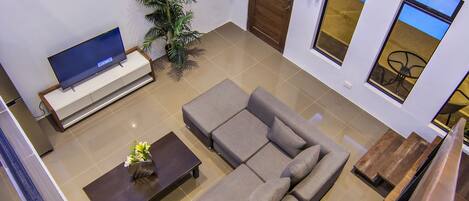 Un salon moderne avec un canapé d’angle, un téléviseur à écran plat, une table basse et une plante en pot.