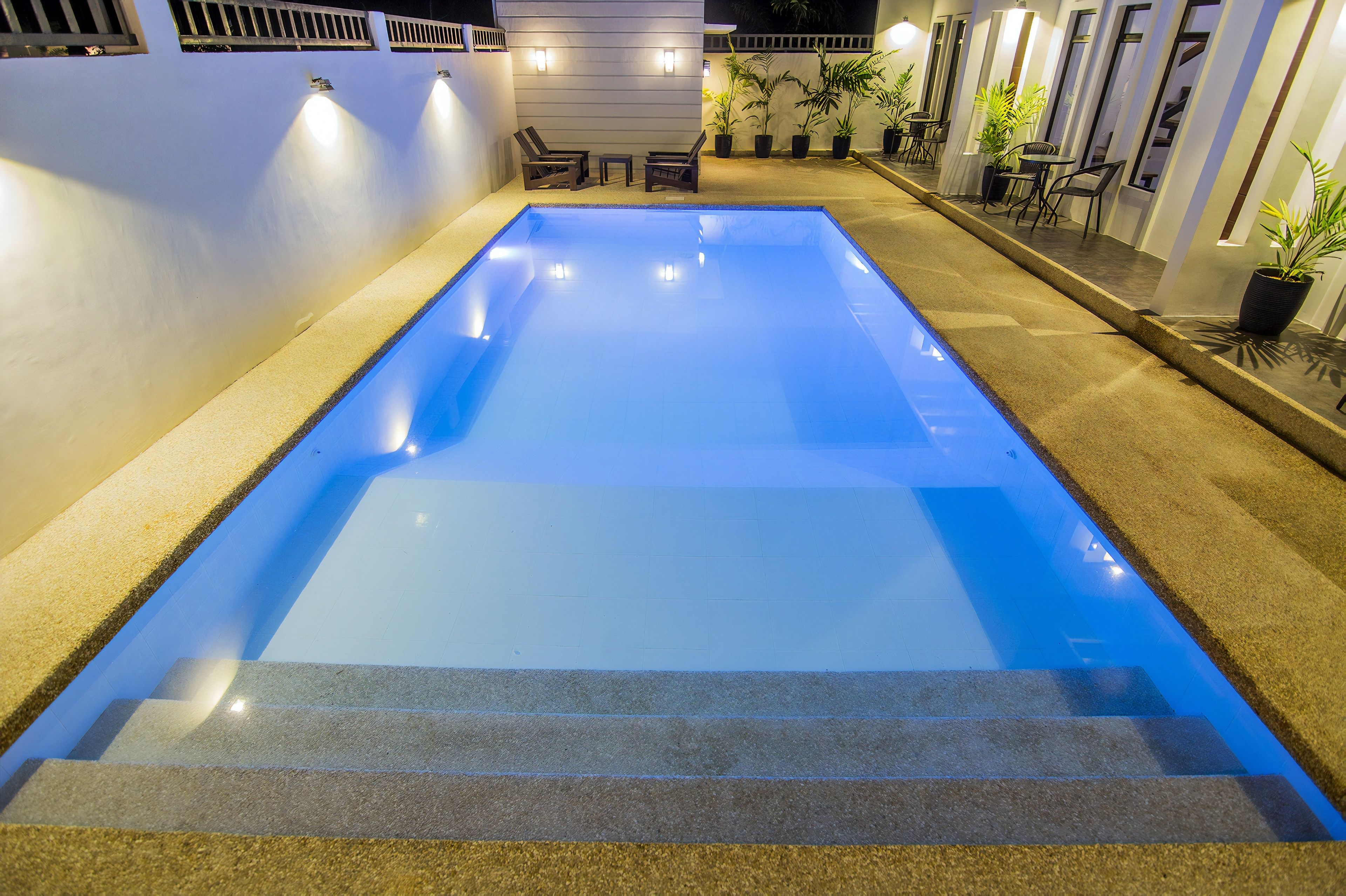 A rectangular swimming pool with steps leading into it, surrounded by a low wall and potted plants.