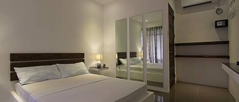Une chambre d’hôtel moderne avec un grand lit, une table de chevet avec une lampe, une armoire avec un miroir et un climatiseur fixé au mur.