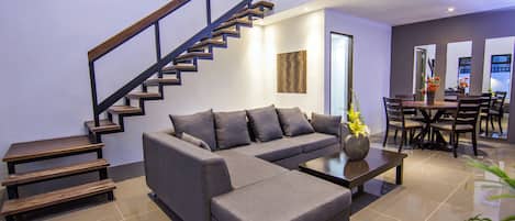 Una sala de estar moderna con un sofá seccional gris, una mesa de centro y una escalera con escalones de madera y barandales de metal.