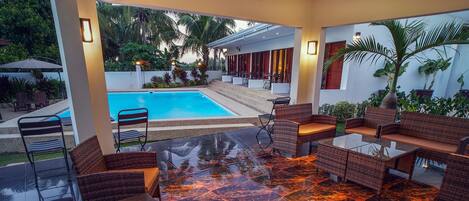Un espacio lounge al aire libre con piscina, mobiliario de mimbre y una mesa de cristal.